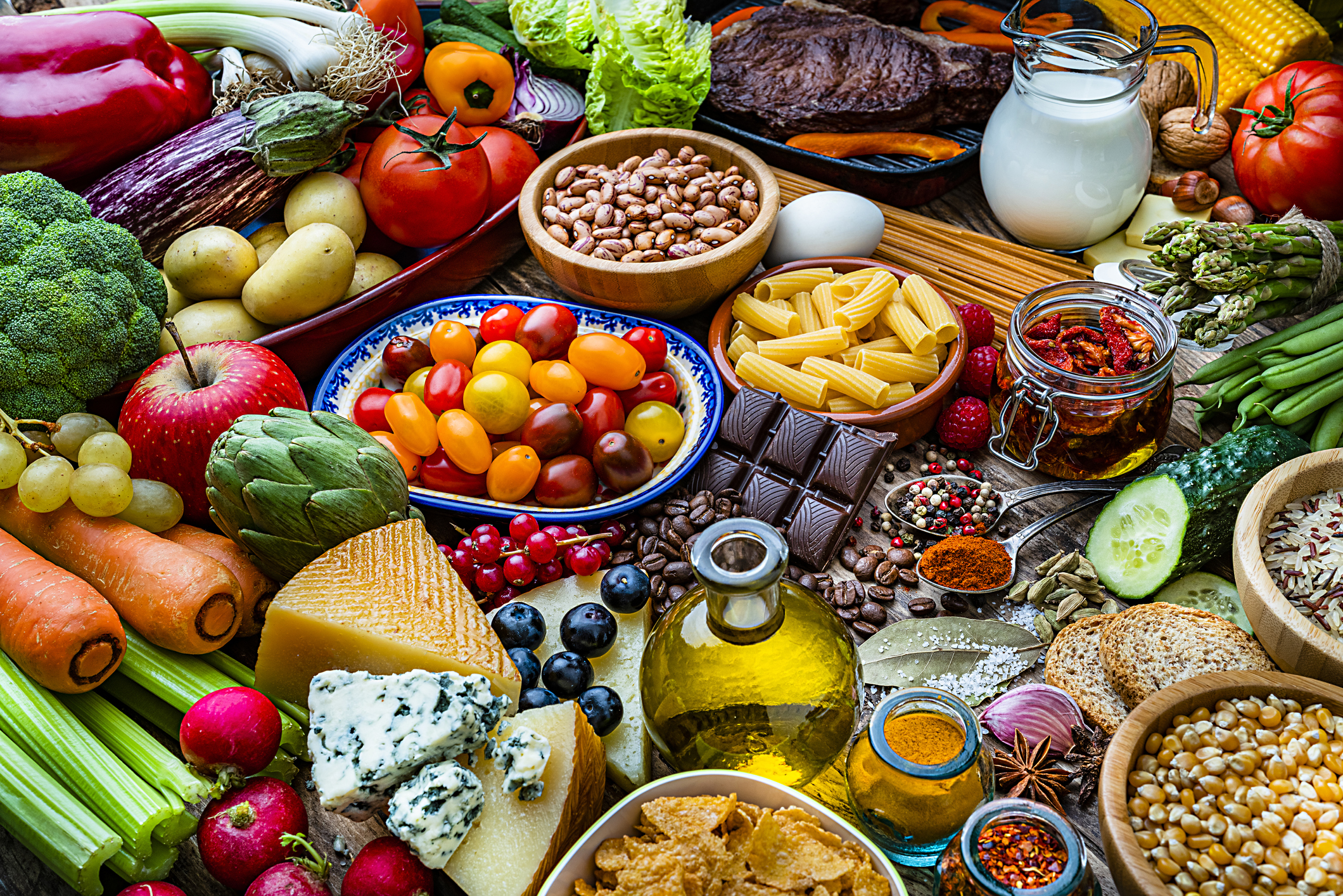 Food and drink backgrounds: high angle view of a wooden table filled with a large variety of food. The composition includes fruits, vegetables, cooking oil, cereal,  dairy products, legumes, spices, herbs, pasta, bread, nuts, cheese, eggs, milk, preserves, chocolate, roasted coffee beans among others. High resolution 42Mp studio digital capture taken with SONY A7rII and Zeiss Batis 40mm F2.0 CF lens