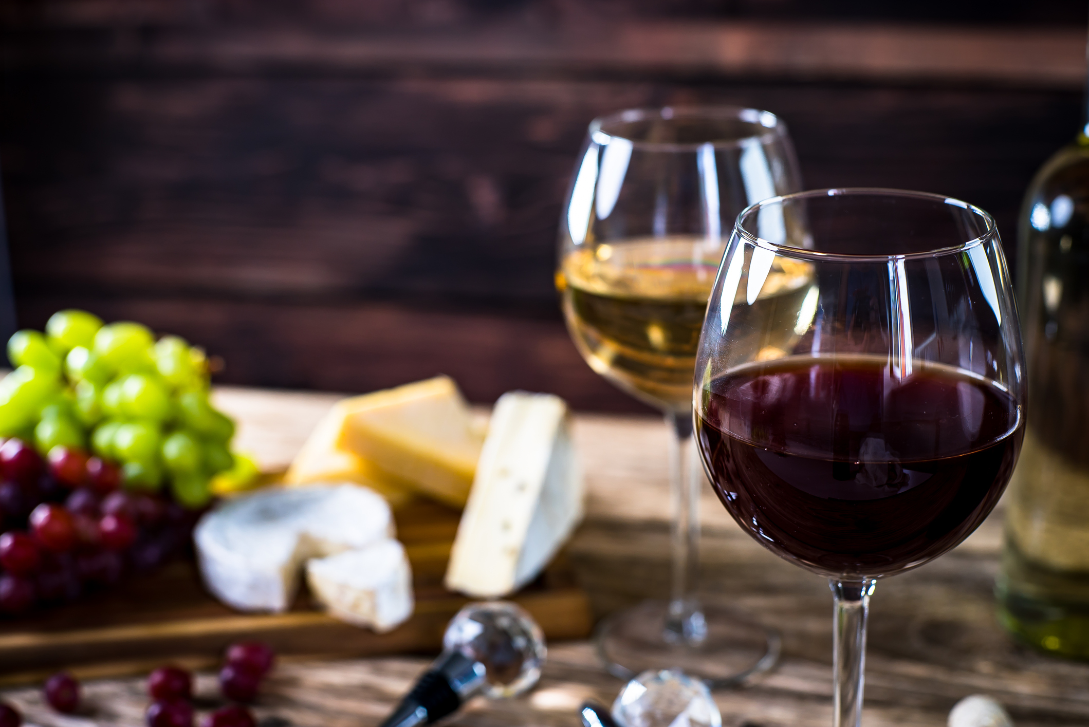 Glass of red wine, cheeses and grapes on brown wooden background