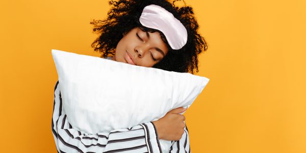 Sleeping. Dreams. Woman portrait. Afro American girl in pajama is hugging a pillow, on a yellow background