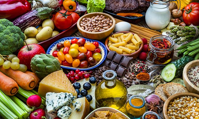 Food and drink backgrounds: high angle view of a wooden table filled with a large variety of food. The composition includes fruits, vegetables, cooking oil, cereal,  dairy products, legumes, spices, herbs, pasta, bread, nuts, cheese, eggs, milk, preserves, chocolate, roasted coffee beans among others. High resolution 42Mp studio digital capture taken with SONY A7rII and Zeiss Batis 40mm F2.0 CF lens